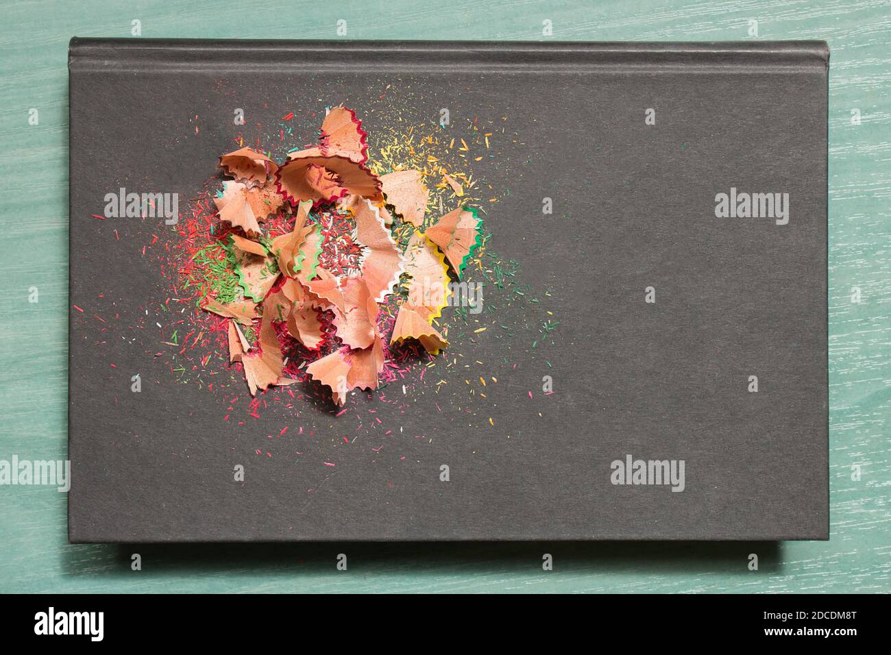 A book with colored pencil shavings on a classroom wooden table. Stock Photo