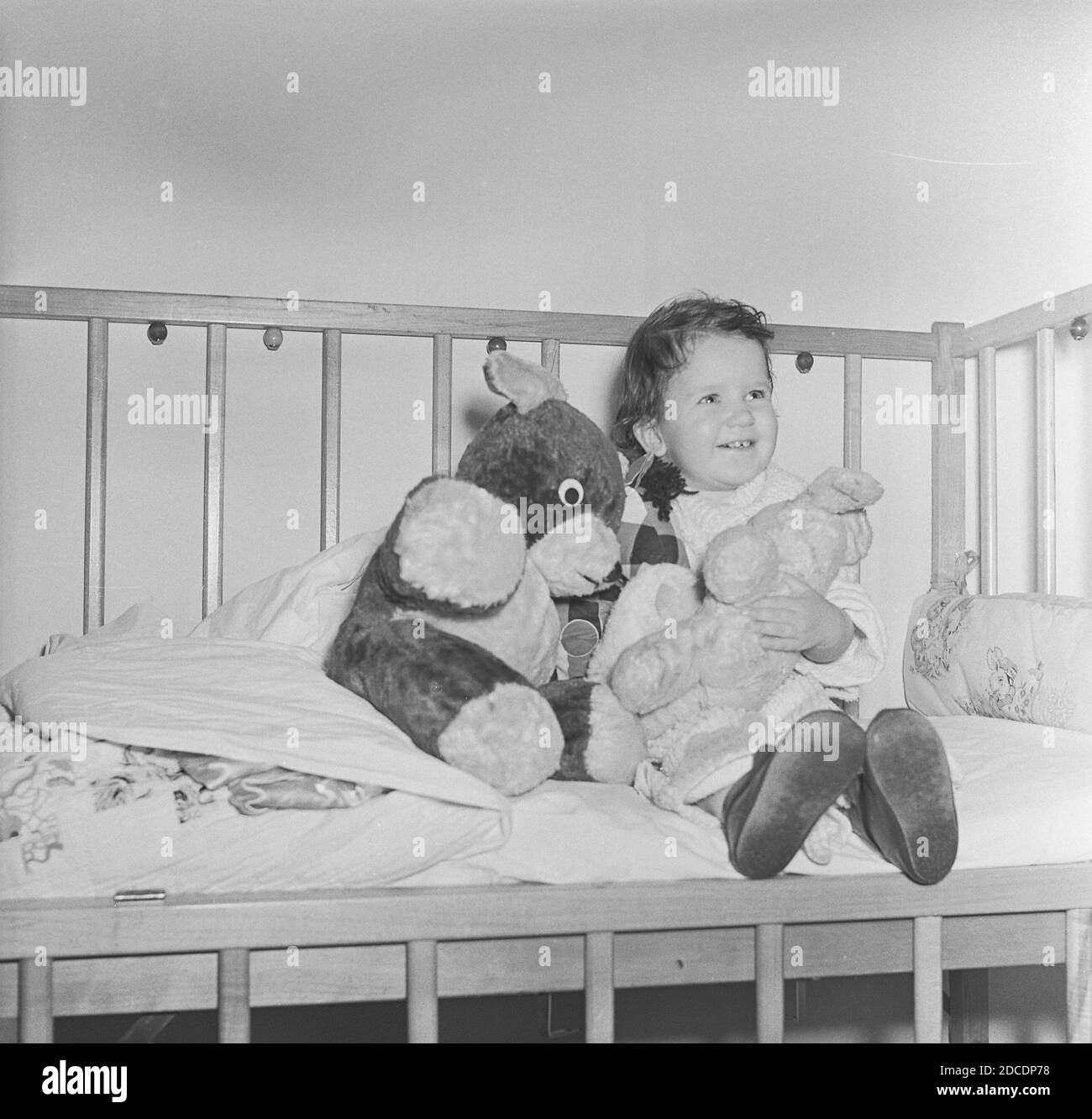 Cute baby girl sits in her crib with her favorite stuffed animals, USA