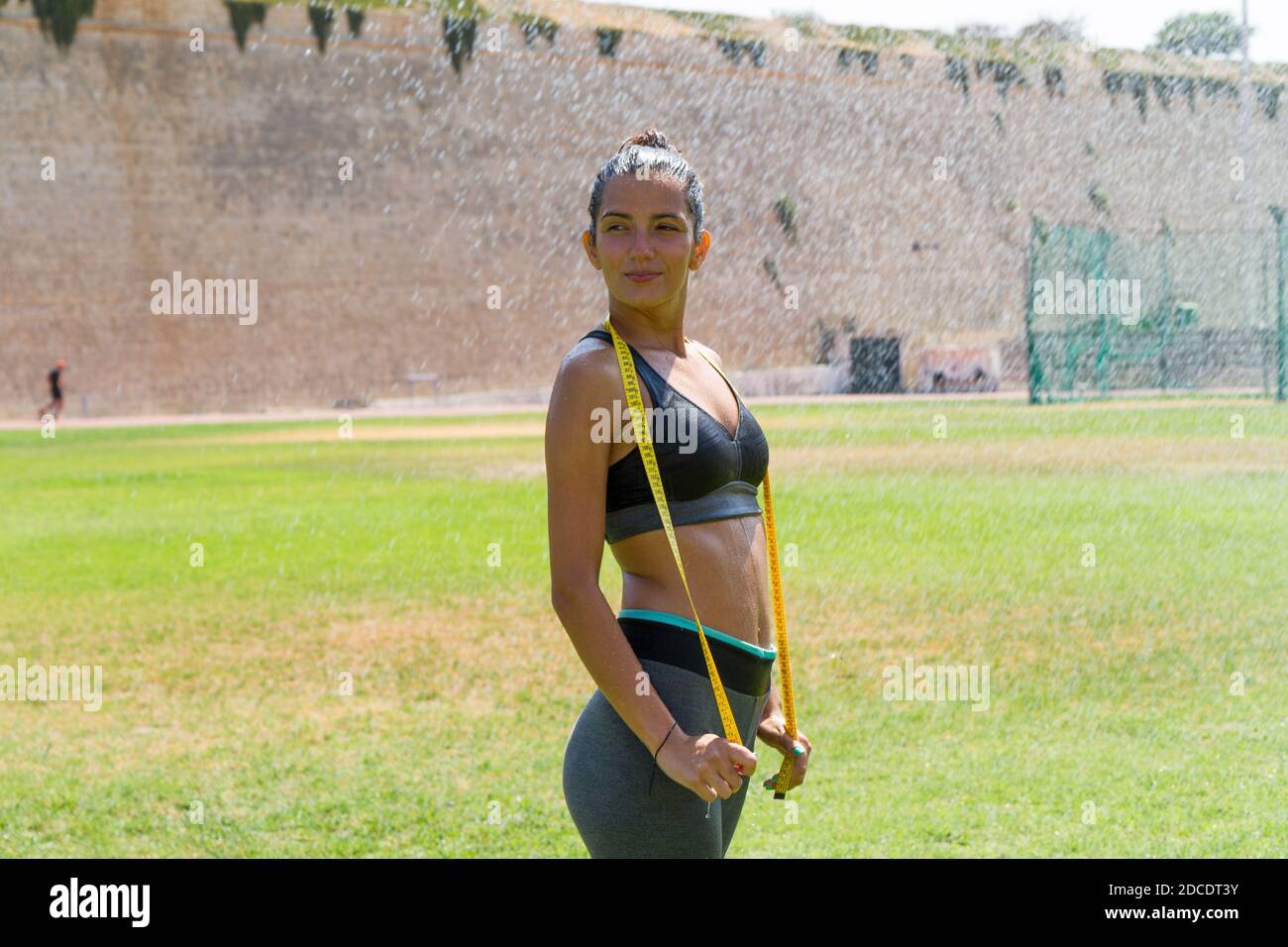 Female water sprinkled wet athlete woman in sportswear measuring her  waistline, hips and chest after a workout at an outdoor field stadium.  Healthy li Stock Photo - Alamy
