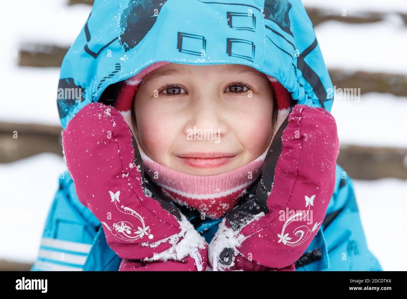 Close-up portrait of cute caucasian baby in winter clothes. A 6-7 year old girl with ruddy cheeks from frost, in winter overalls and mittens Stock Photo