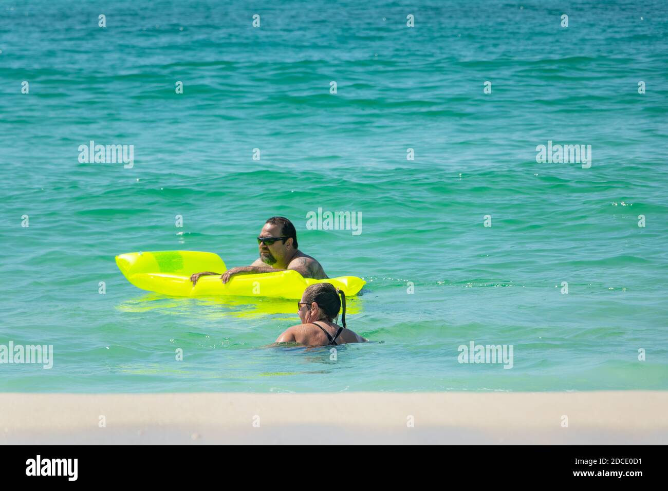 couple swimming in green sea with fluorescent lilo inflatable at beach at Biloxi Mississippi USA