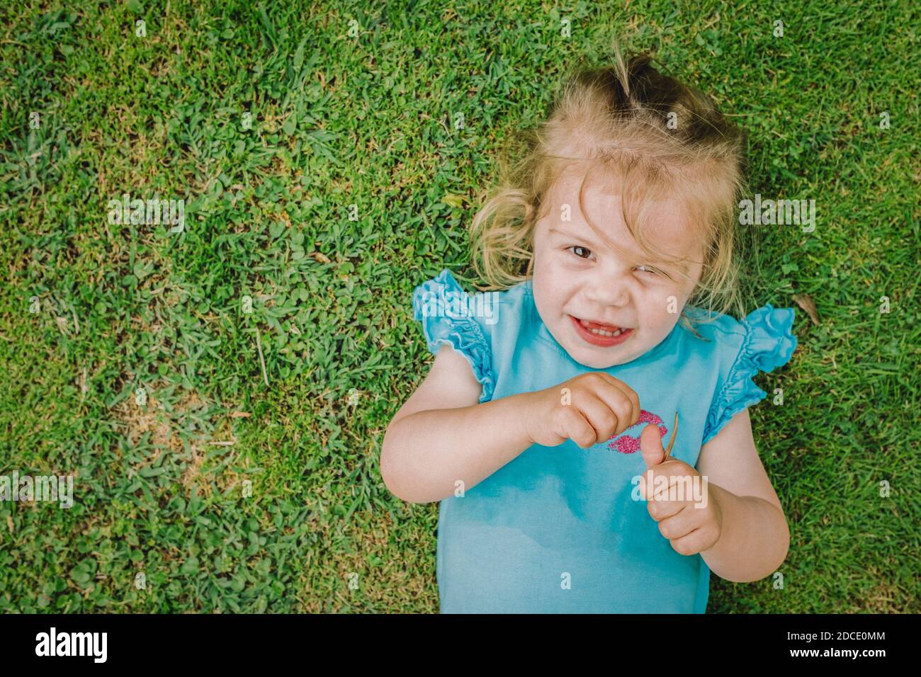 Two year old girl lying upside up smiling and on the grass turf in the garden on a beautiful spring day Stock Photo