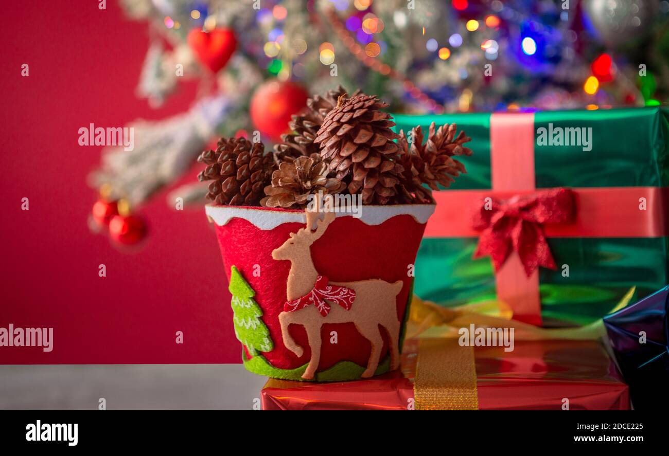 Pot decorated in red and green, with reindeer and pine full of pine-codes and in the background a Christmas tree with balls hearts snow lights. Stock Photo