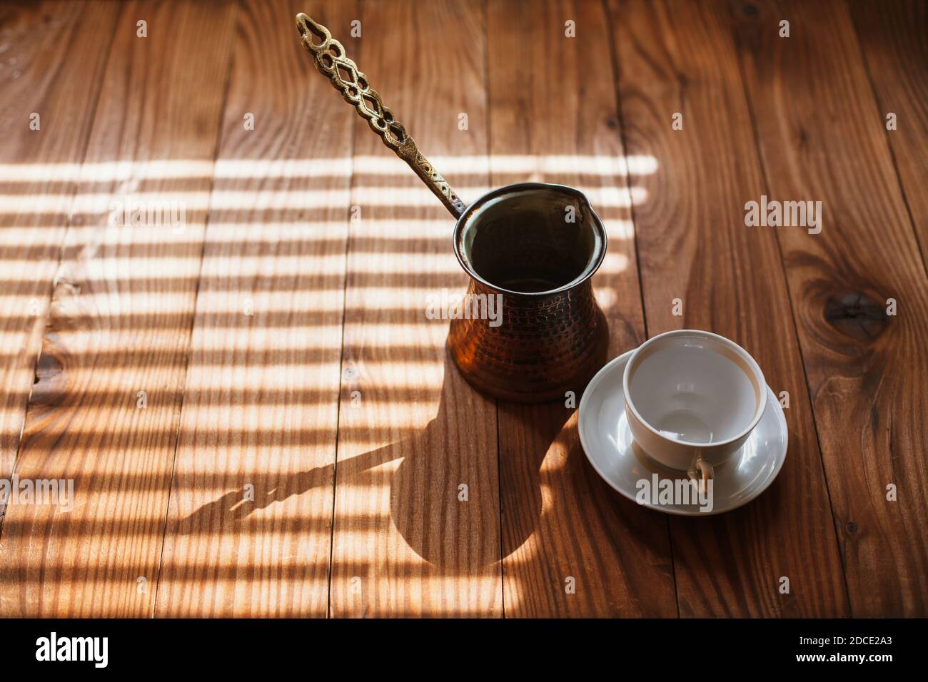Traditional copper turkish coffee pot, cezve, ibrik and empty white porcelain cup with saucer, on a wooden table, closeup. Stock Photo