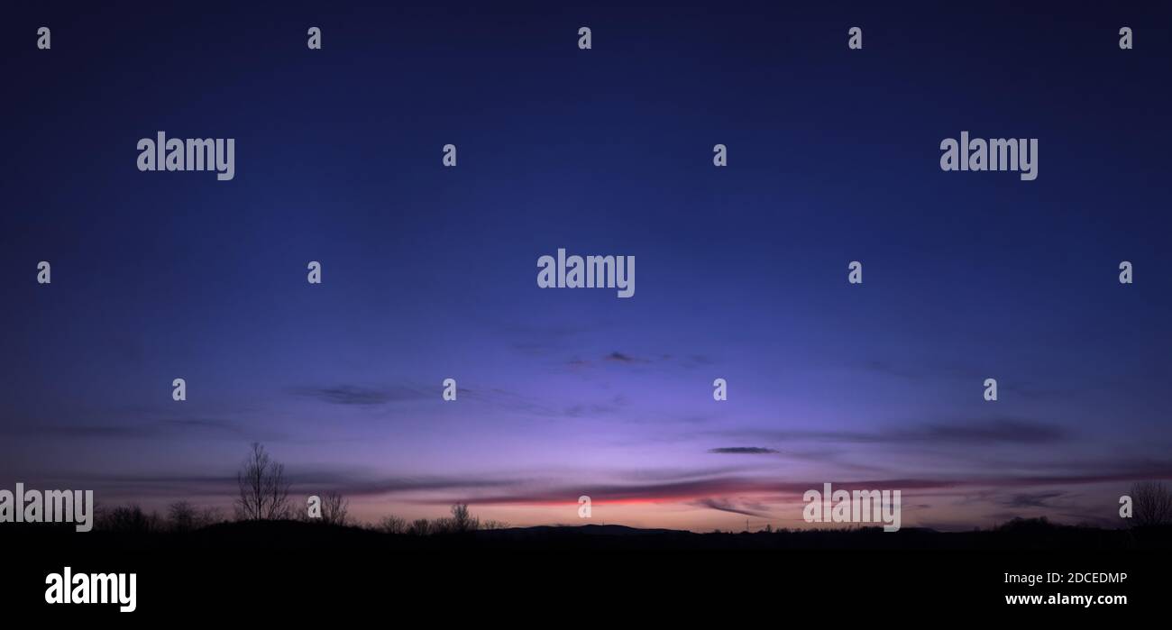 Beautiful blue, purple and orange gradient sky during sunset in the early spring. Tree silhouettes, stitched panorama. Stock Photo