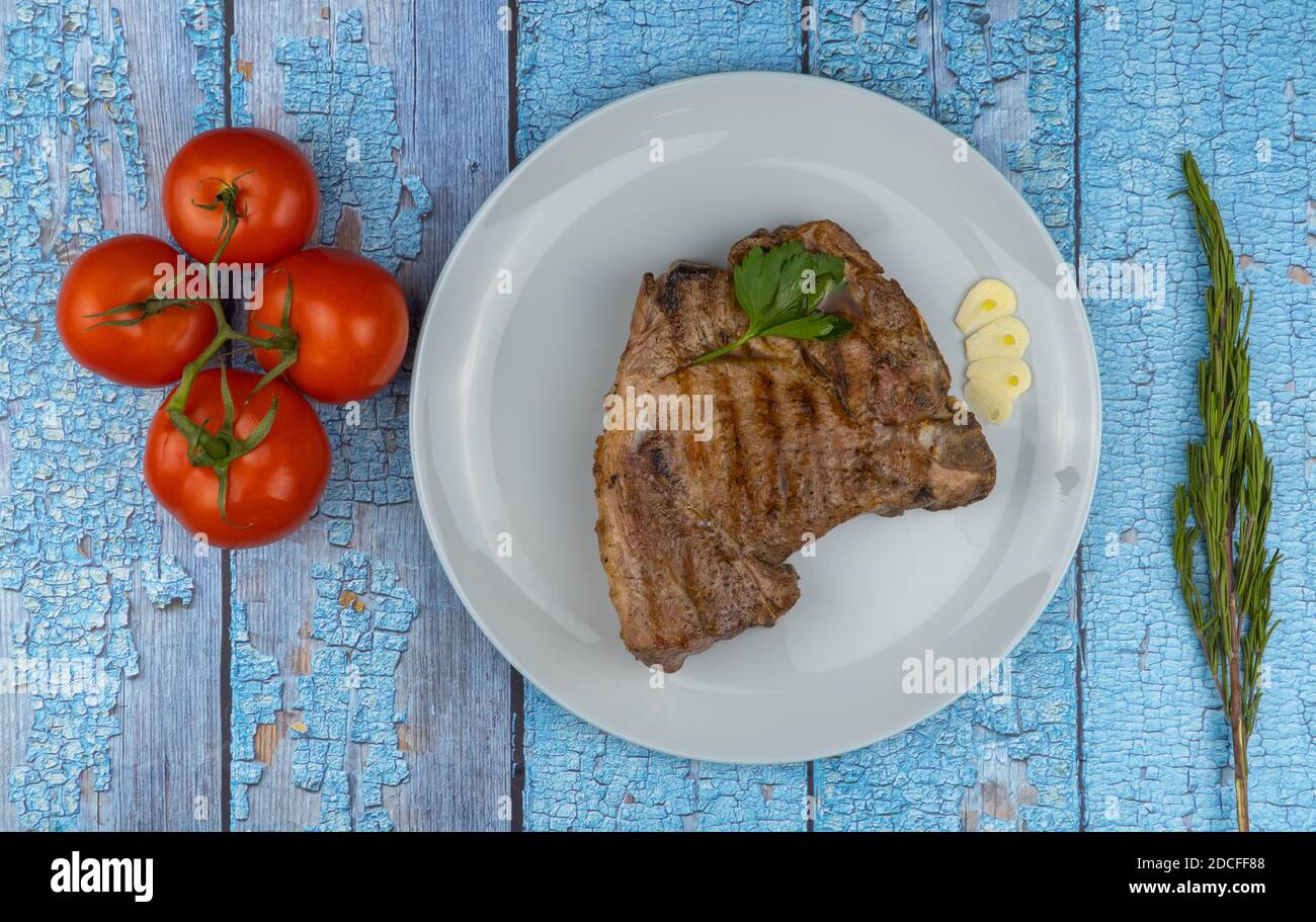 piece of delicious pork. fried steak in a plate on a wooden background. piece of deep-fried meat with tomatoes and a sprig of rosemary. Stock Photo