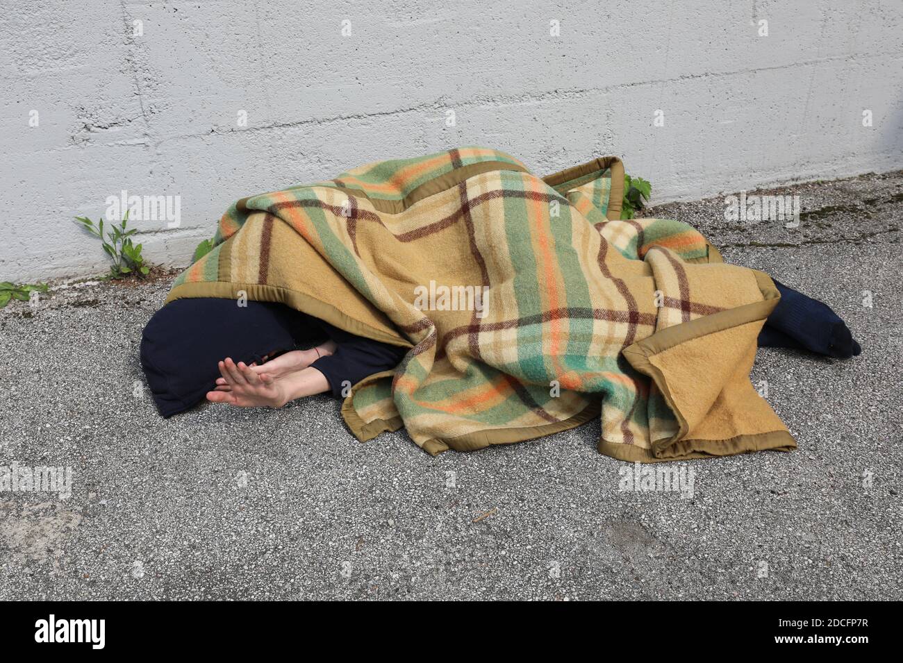 homeless as he sleeps on the floor under a blanket and hoodie Stock
