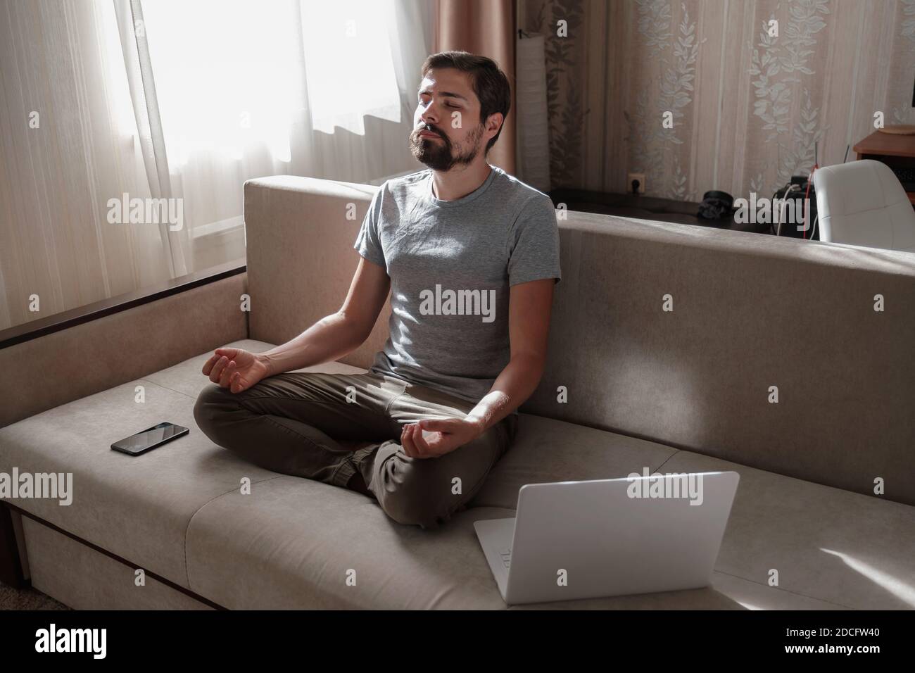 millennial hipster guy enjoy no stress peace of mind lounge on sofa at home. Men do meditation with laptop and phone on sofa Stock Photo
