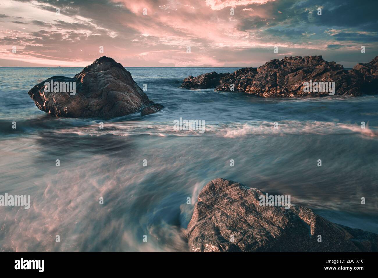 Silky water and dramatic sunrise with rocks on the beach of Sant Pol de Mar, Catalunya, Spain Stock Photo