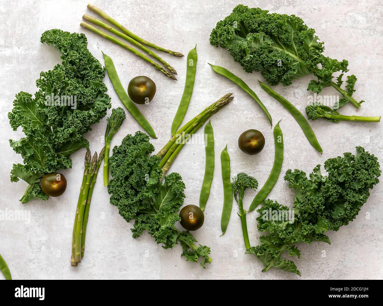 A healthy spread of fresh raw green vegetables. broccolini, kale, peas, beans, lettuce, tomatoes.  Stock Photo