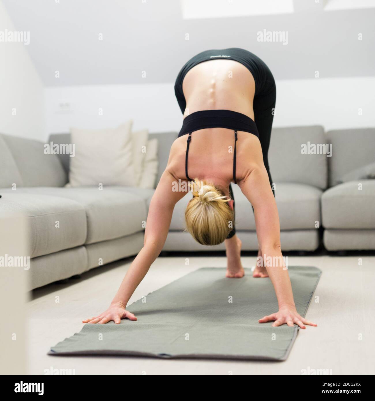 Beautiful blonde woman doing home workout indoors. Woman practice yoga at home. Fit girl using workout tutorials for healthy active lifestyle. Woman Stock Photo
