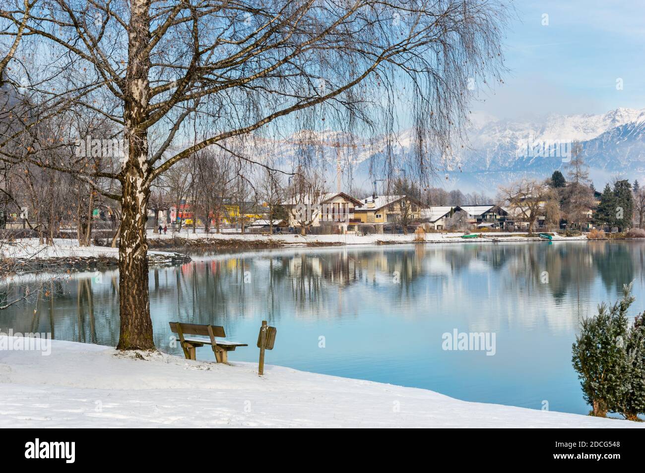 Zell am See in winter. View from Esplanade over Lake Zell to Prielau town. Idyllic scene with bank, birch tree, snow and misty mountain in alpine town Stock Photo