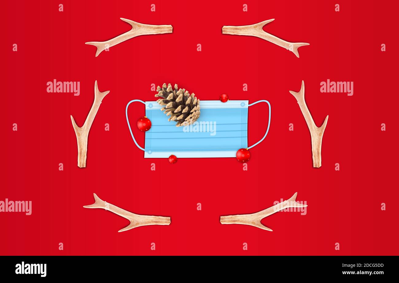covid-19 festive christmas concept. mask face and pine cone elements with horns deer decoration. flat lay on red holiday background Stock Photo