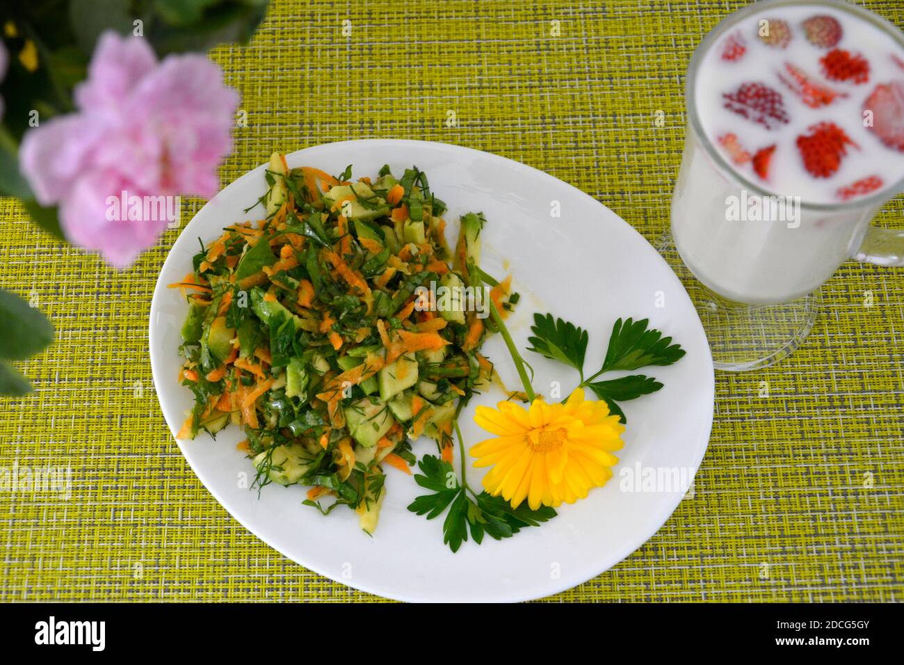 A salad of fresh vegetables is decorated with a nasturtium flower and a glass of milk and strawberries on a green napkin. Vegetable salad for diet foo Stock Photo