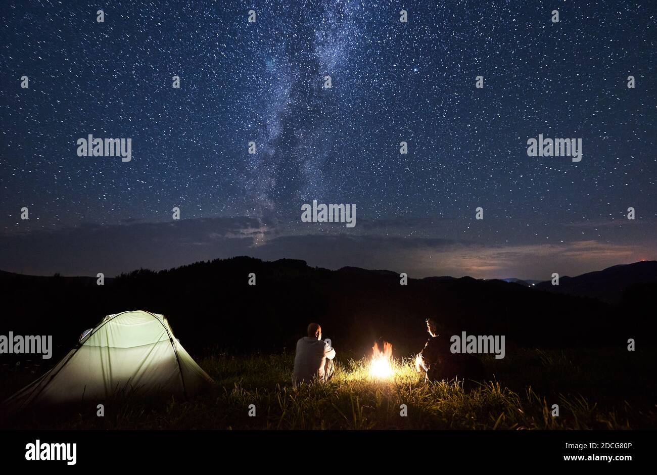 Couple of friends sitting around a campfire in the mountains in summer ...