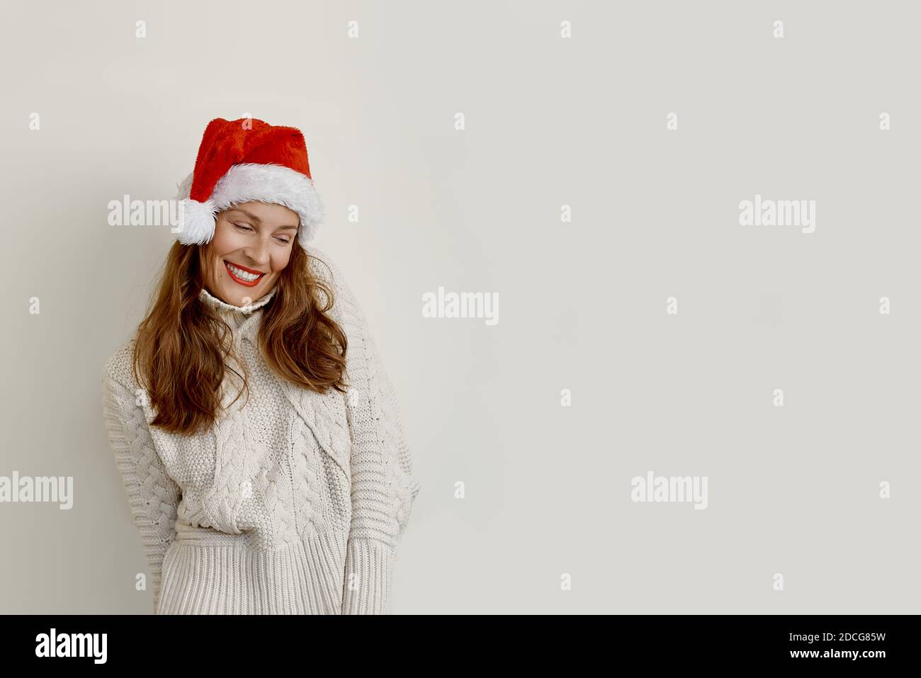 Woman wearing a sweater and a santa hat looking down and smiling Stock Photo