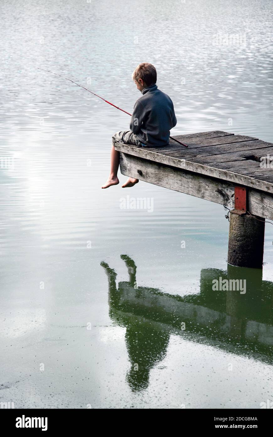 Small boy fishing in pond with cane rod and reflection while