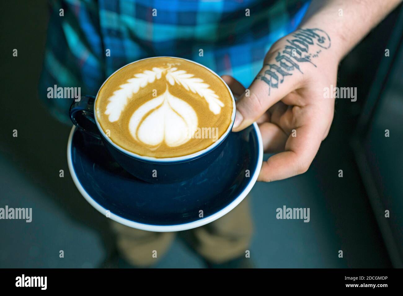 GREAT BRITAIN / England / London/Hand with tatoo holding coffee cup in an indoor cafe in London.Close up of hands holding cup of coffee. Stock Photo
