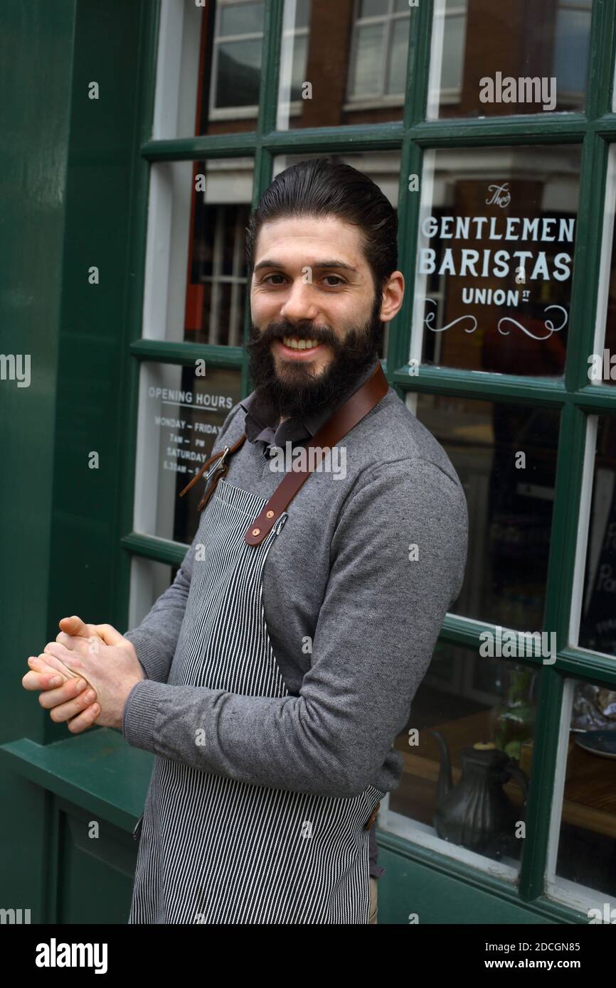 Successful Male Barista standing on front of the coffee shop. Portrait of Beard barista with apron in front of cafe Stock Photo