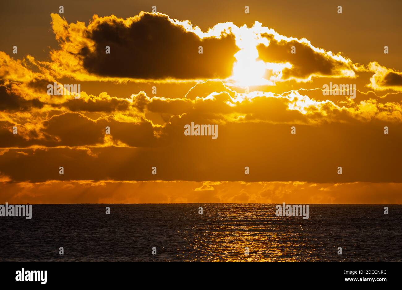 Sunset at sea. Landscape view of the low sun going down over the ocean with cloudy sky, in the UK. Stock Photo
