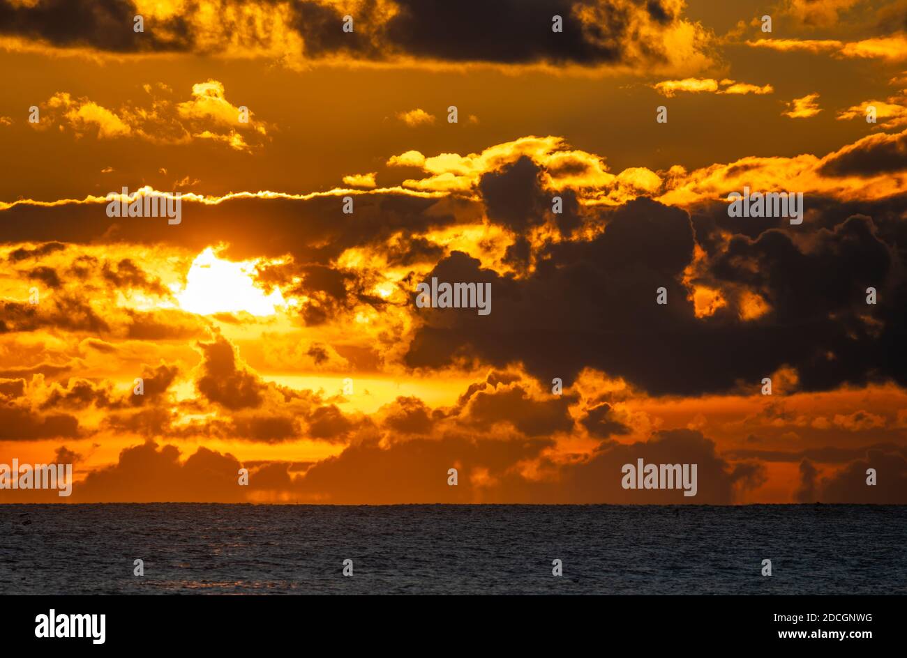 Sunset at sea. Landscape view of the low sun going down over the ocean with cloudy sky, in the UK. Stock Photo