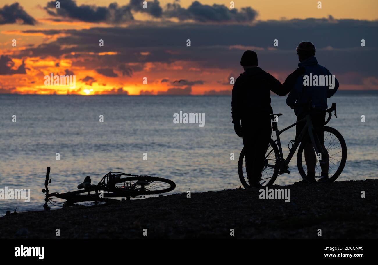 Silhouettes of a pair of people (male) illustrating Father and Son family concept, on a beach watching a sunset, as the sun goes down over the sea. Stock Photo