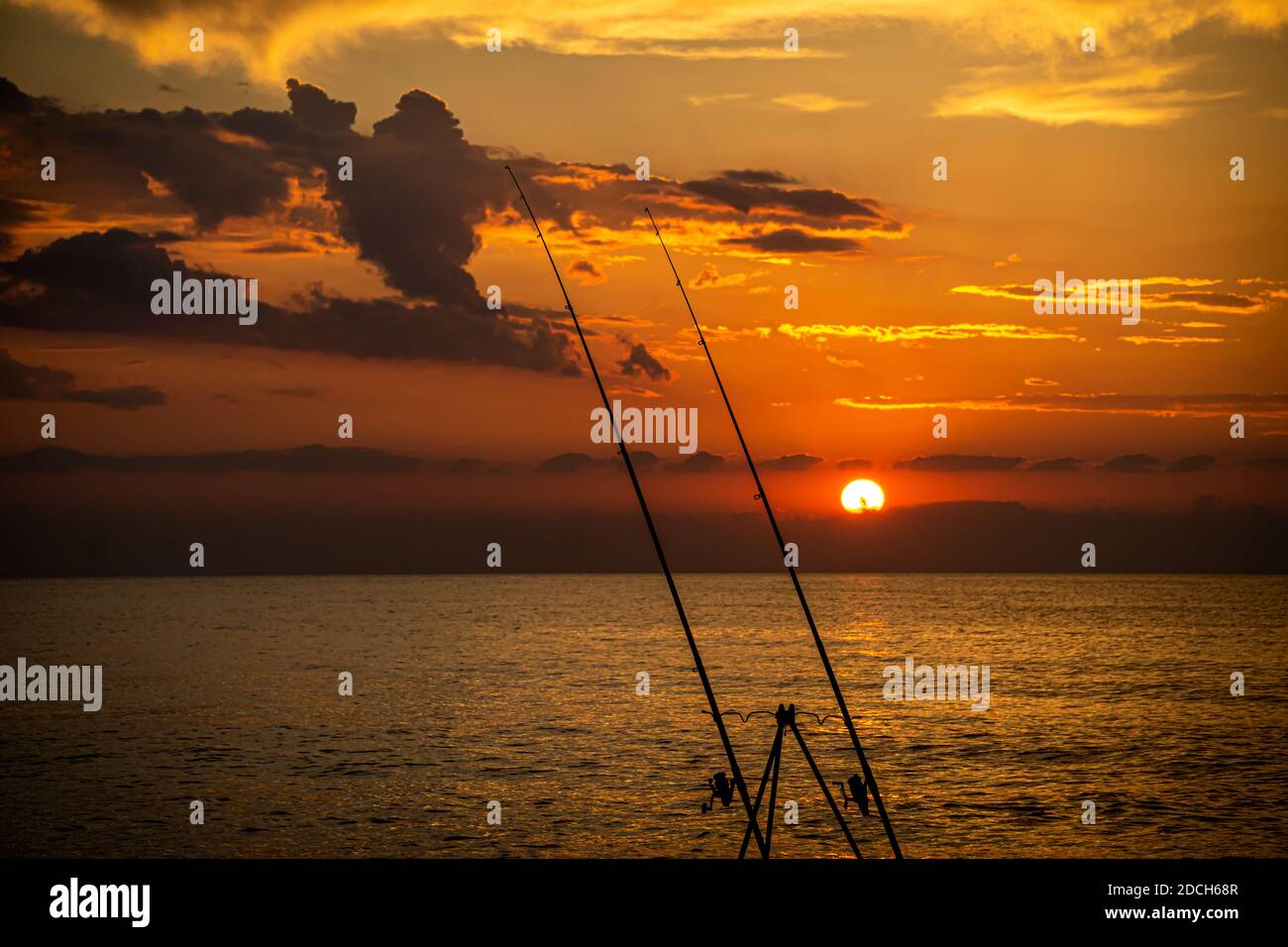 frontal view of sunset over the sea with two fishing rods in the foreground Stock Photo