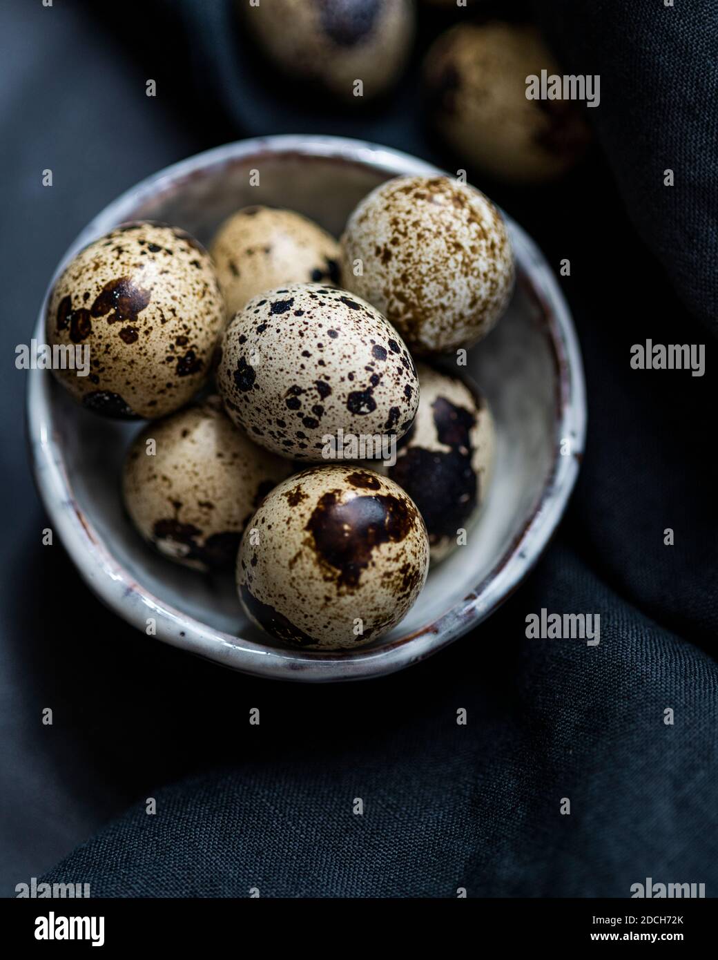 Quail eggs in white bowl on black backdrop, quail eggs, pile of quails eggs in bowl, speckled eggs, speckled eggs in bowl, quail eggs dark background Stock Photo