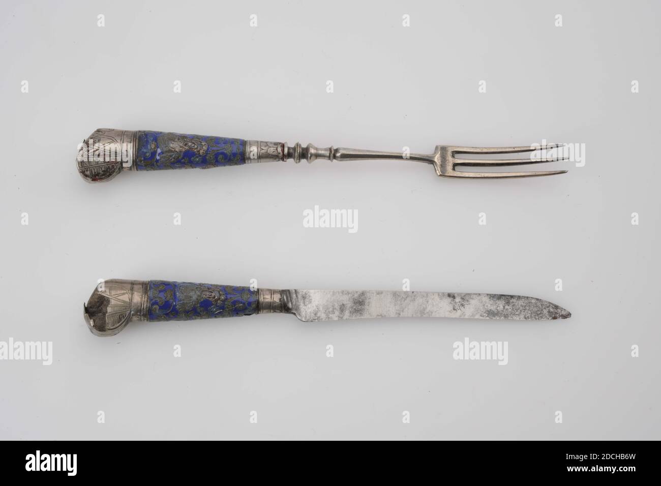Anonymous, first half 18th century, leather, rayskin, silver, iron, enamel, sheath: 22 x 3.4 x 2.9cm 220 x 34 x 29mm, knife: 15.8 x 1.9 x 1.3cm 158 x 19 x 13mm, Fork: 15.9 x 1.9 x 1.3cm 159 x 19 x 13mm, weapon sign, Silver fork and iron blade with an enamelled handle, partly covered with silver fittings. A minerva bust between tendrils and flower vases and silver inlay are depicted on the handle. At the ends a silver button in which a weapon is engraved, with cross stripes on the left and two crossed swords on the right. The knife and fork are in a leather sheath with a loose cap, which is Stock Photo