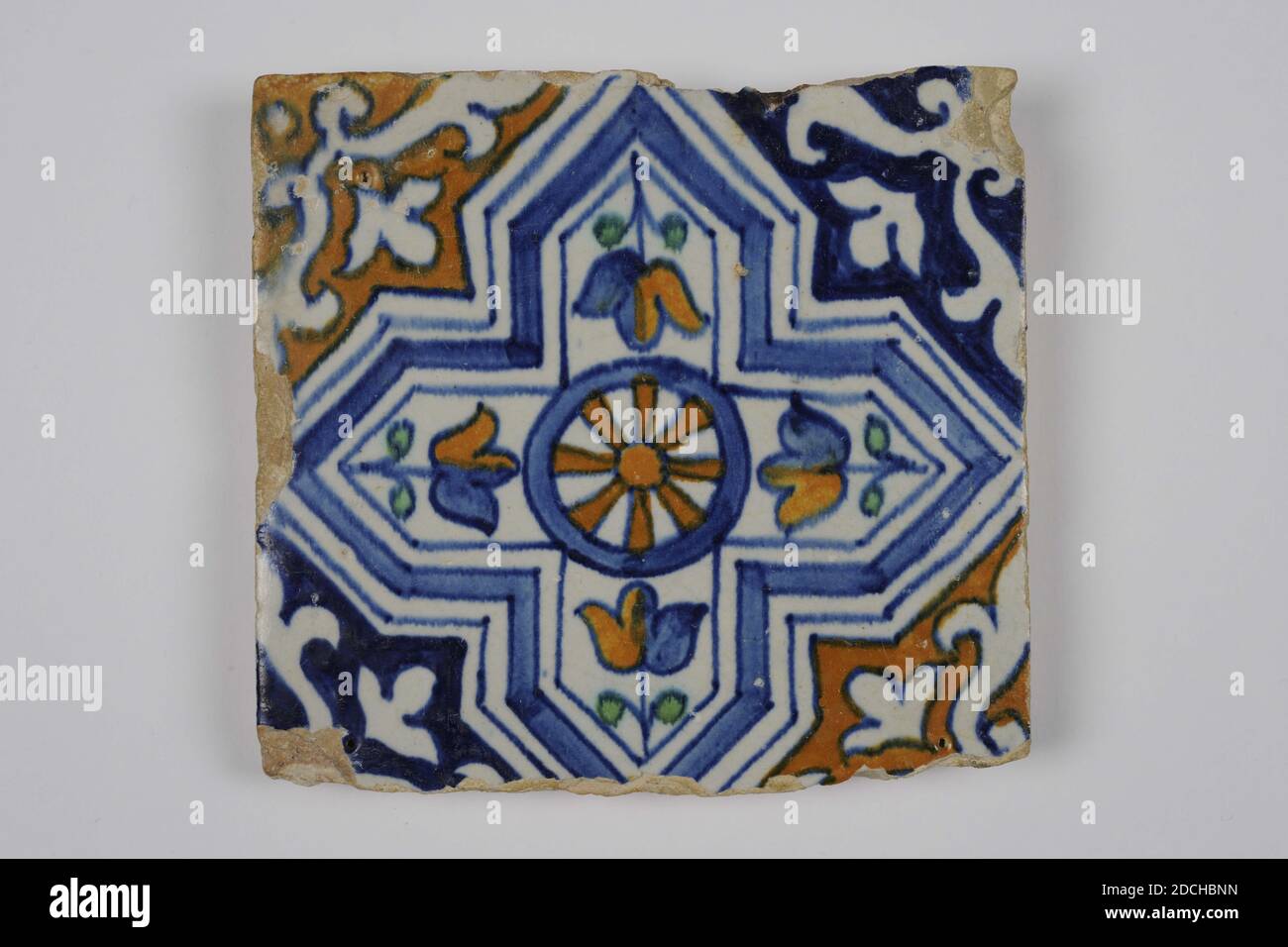 wall tile, Anonymous, c. 1600, tin glaze, earthenware, General: 12.5 x 13.3 x 1.8cm (125 x 133 x 18mm), wheel, tulip, Northern Netherlands, Ornament tile of earthenware covered with tin glaze. Multicolored painted in blue, orange brown and green with a stylized geometric image. The image consists of a straight pointed arch with squared corners. In the center an eight-spoke wheel surrounded by four inwardly directed tulips, 1985 Stock Photo