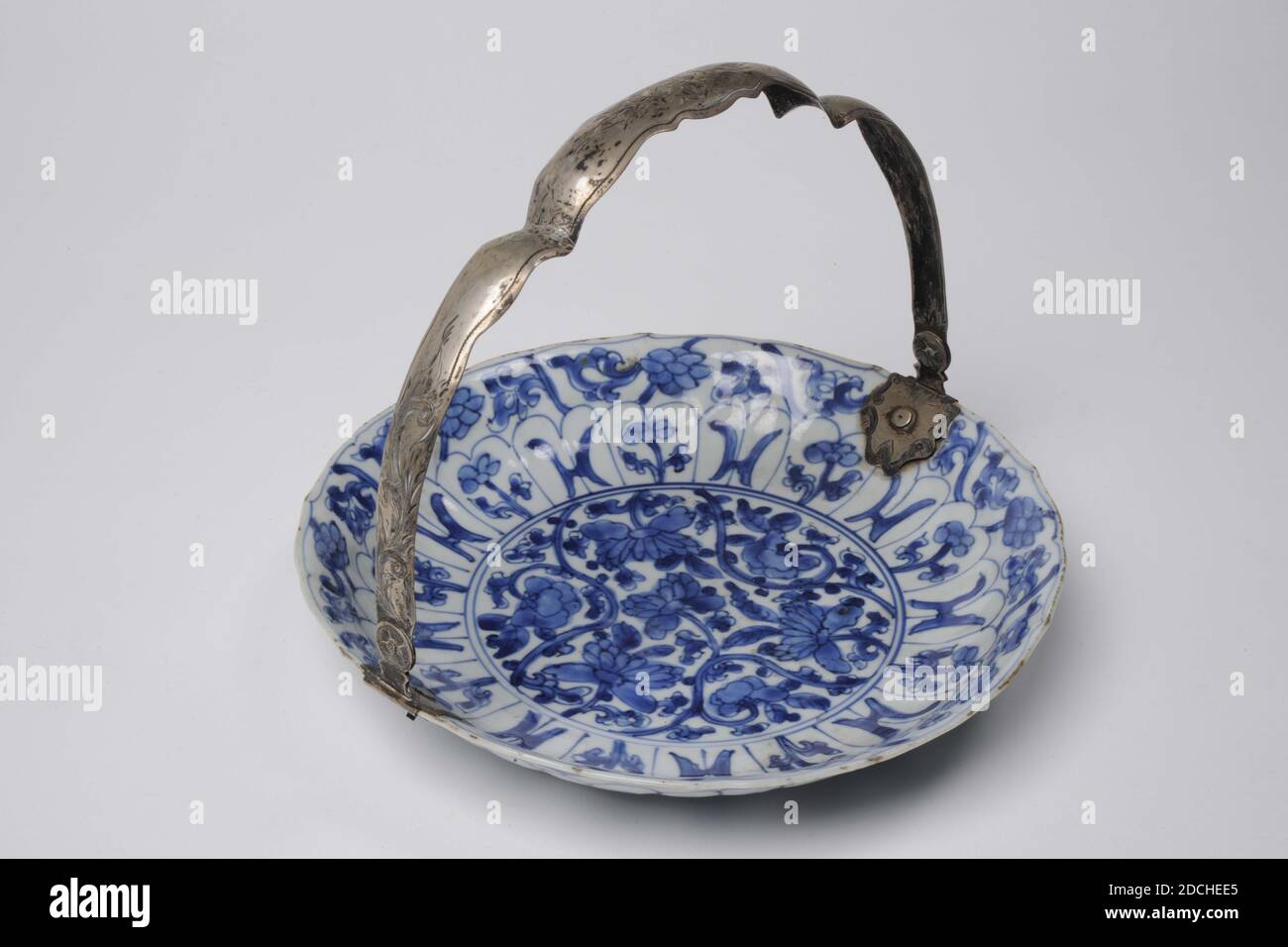 bowl, Anonymous, mid 18th century, porcelain, enamel, silver, Bowl: 3.7 x 21cm (37 x 210mm), With handle (up): 16 x 21 x 21.3cm (160 x 210 x 213mm), flower, Chinese porcelain dish decorated in underglaze blue. The bowl has a silver handle in an arc shape with two kinks. The bowl is decorated in the center with a flower decoration in a circular shape surrounded by eight H-shapes and flowers. The handle is decorated with engraved leaves and flowers. On the back along the edge are signs of Buddhist valuables and H-shapes. In the center a mark in a circle, 1969 Stock Photo