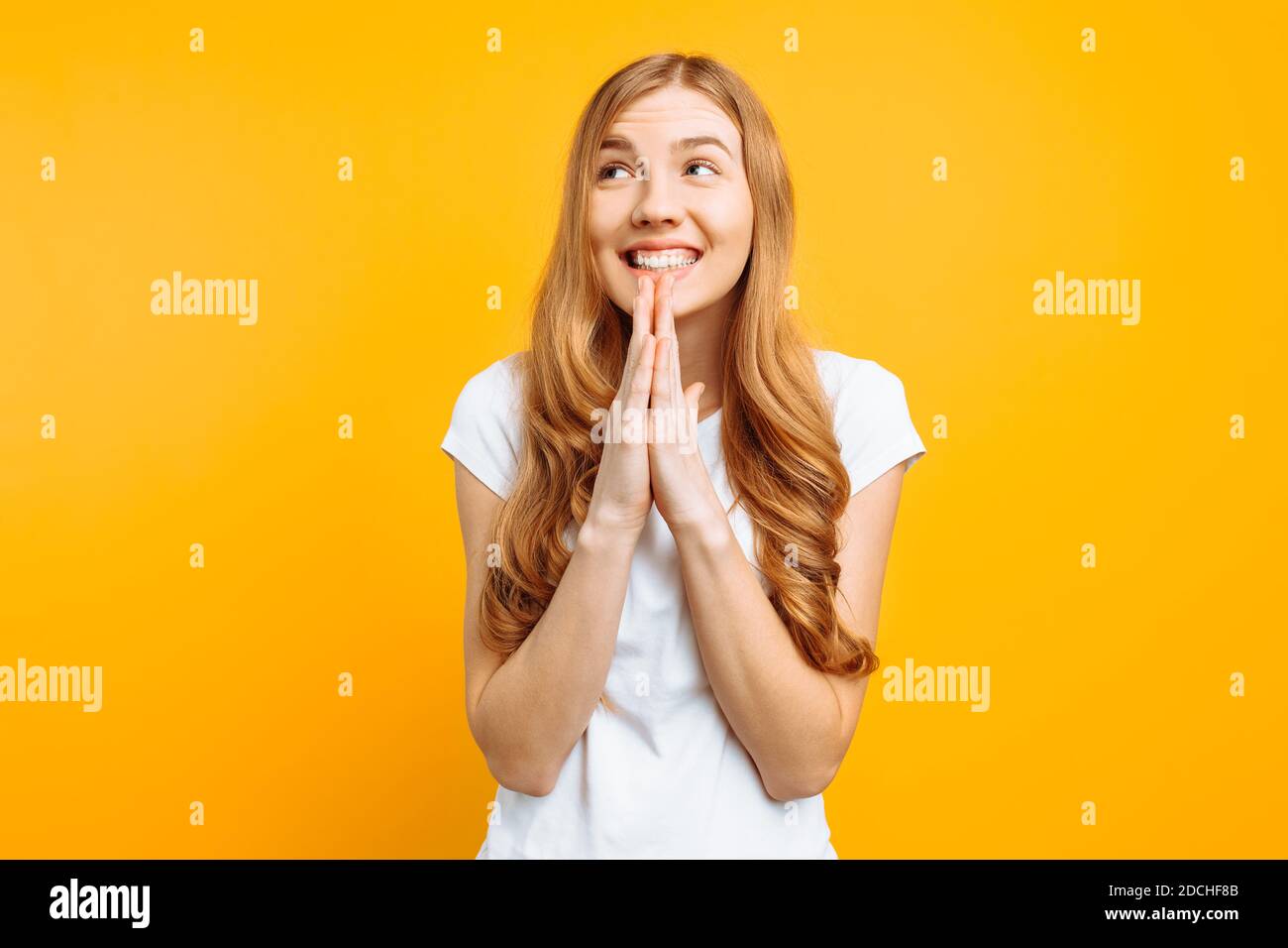 Young focused girl asks God to help her, holding hands near her face, wishes good luck, on a yellow background Stock Photo