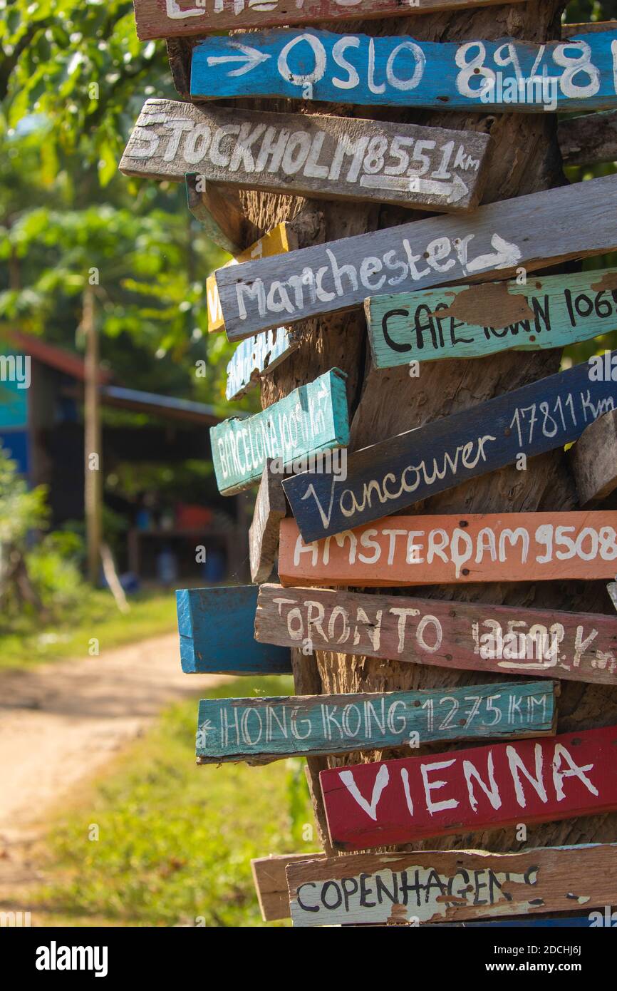 Colourful hand painted direction wood signs to different cities of the world, and mileage marker in Don Det island, one of the famous Four Thousand Is Stock Photo
