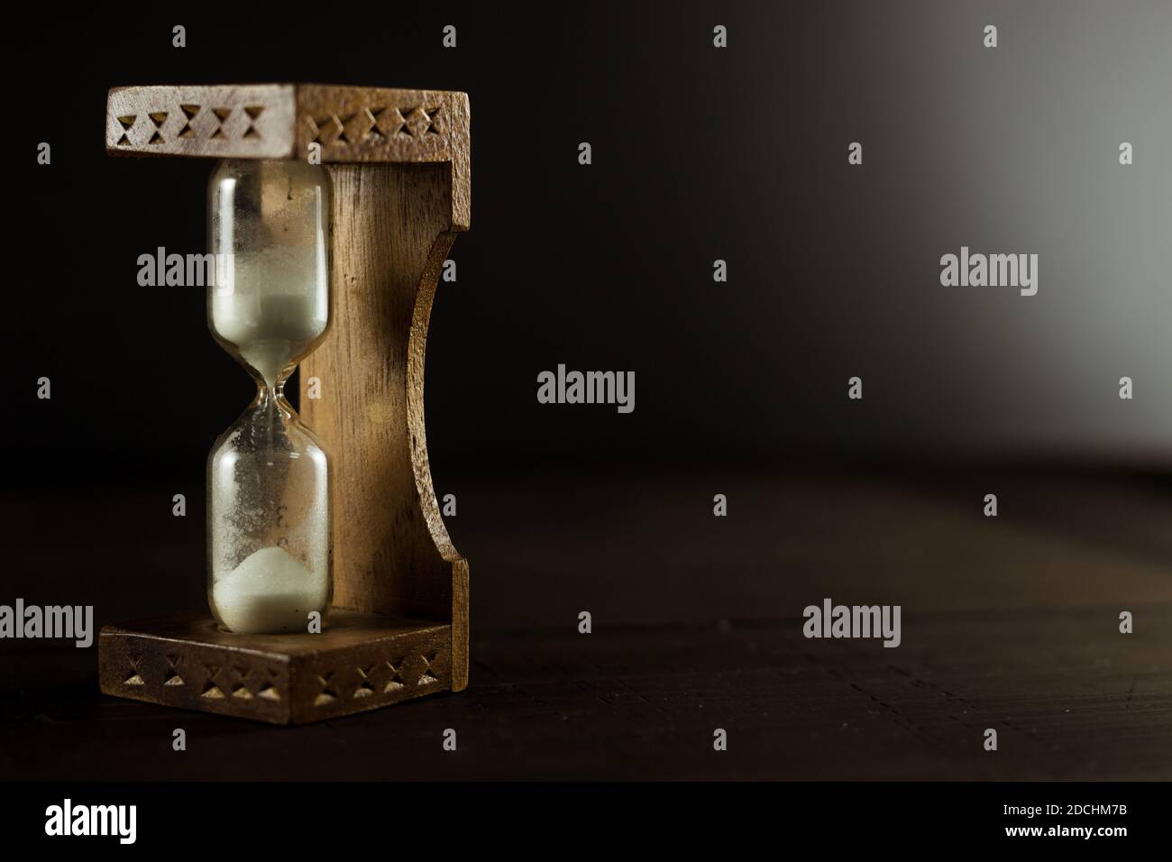 An old vintage hourglass sandglass with white sand on the wooden table. Black background, close up, business deadline concept. Stock Photo