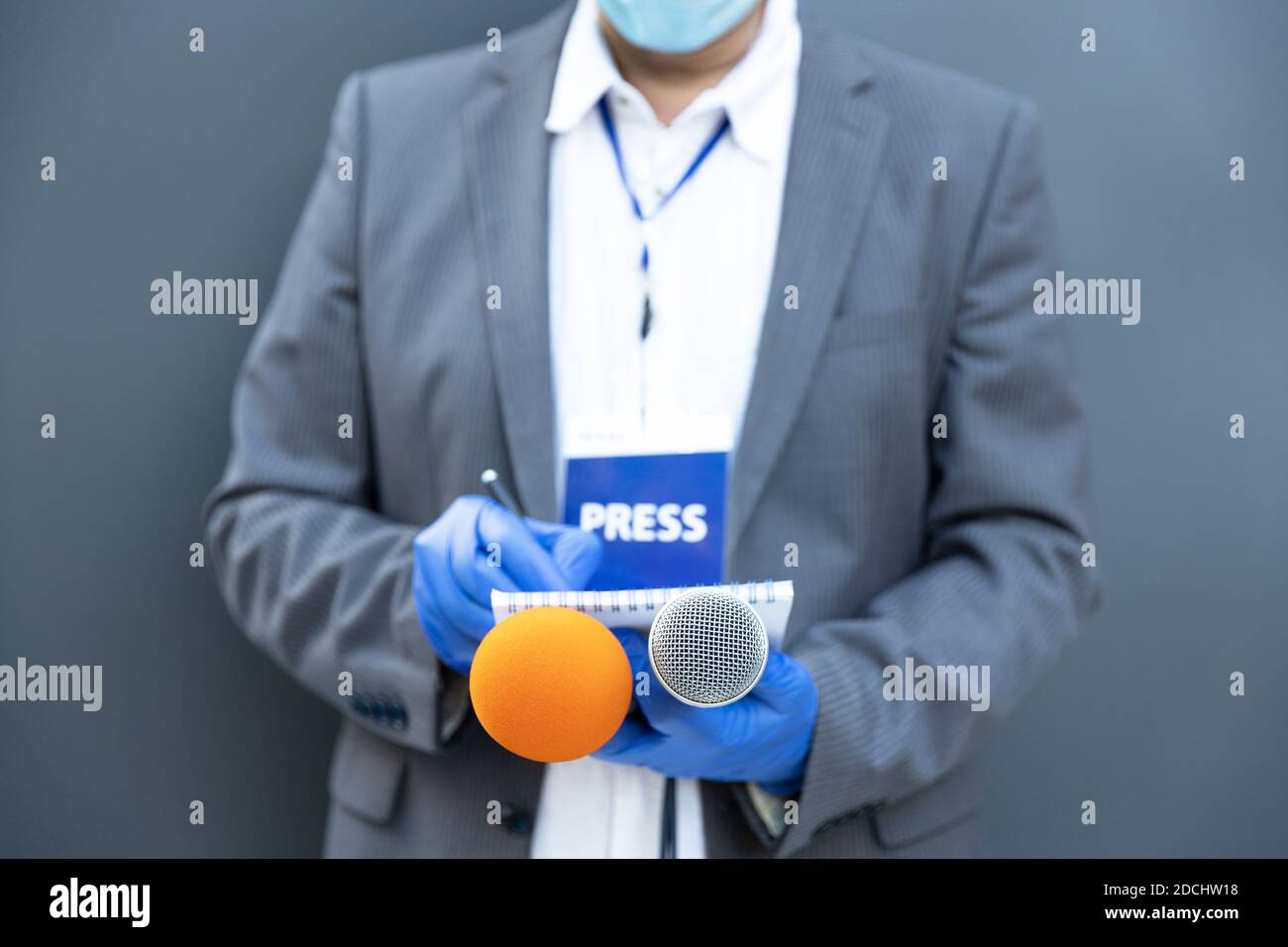 Journalist at news conference or media event wearing protective gloves and face mask against coronavirus COVID-19 disease holding microphone writing n Stock Photo