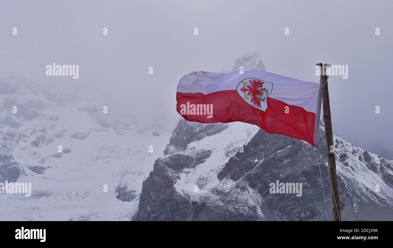 Red and white colored flag of Tyrol with heraldic animal (eagle) flying in wind near mountain refuge Schaubachhütte. Stock Photo