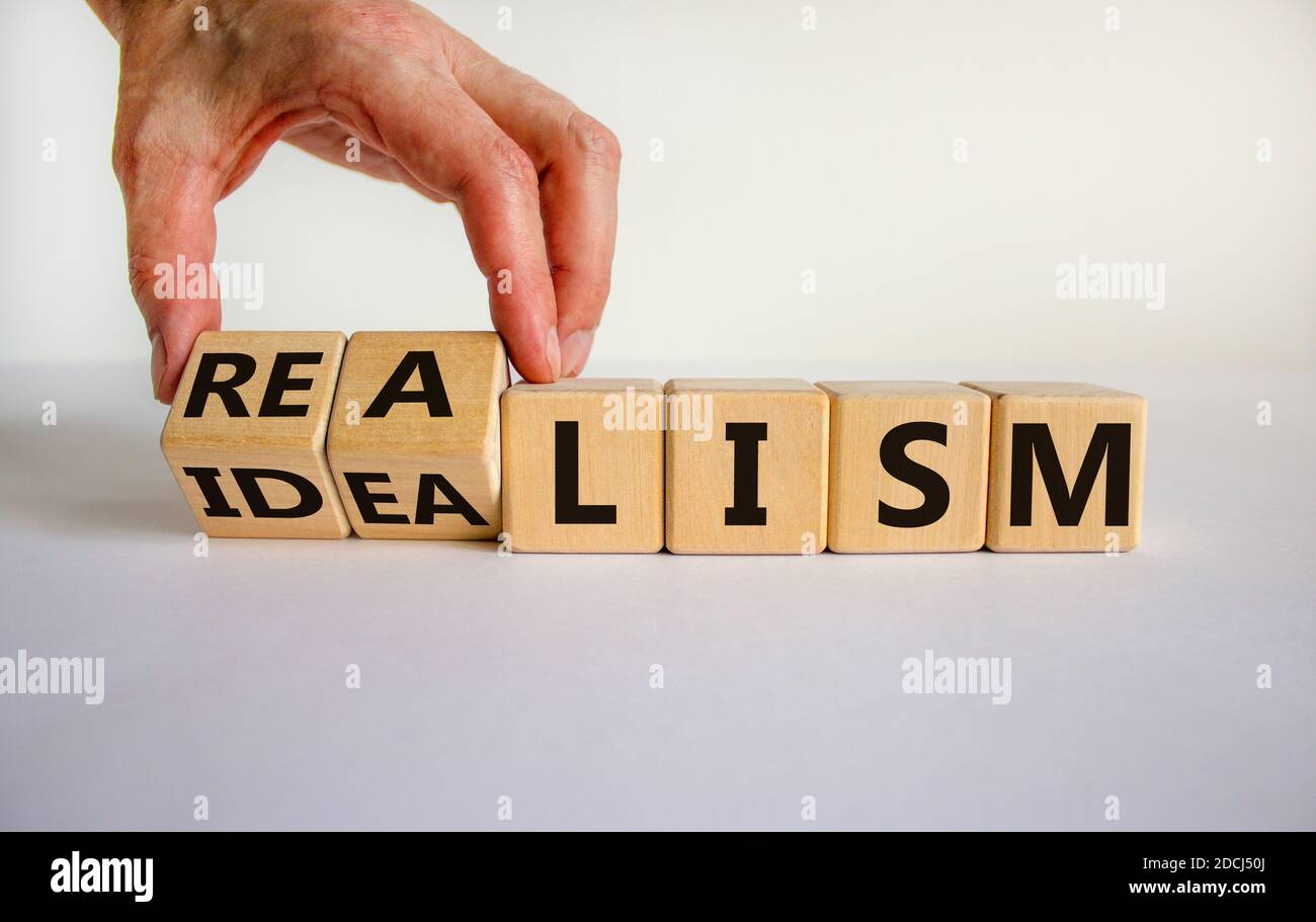 Male hand turns cubes and changes the expression 'idealism' to 'realism' or vice versa. Beautiful white background. Business concept. Copy space. Stock Photo