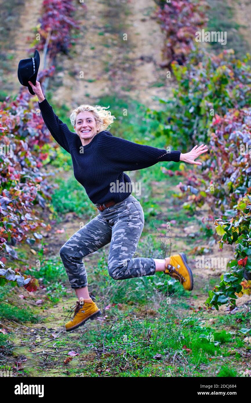 Joyful mature young blondy farmer woman jumping in a vineyard farmland. Stock Photo