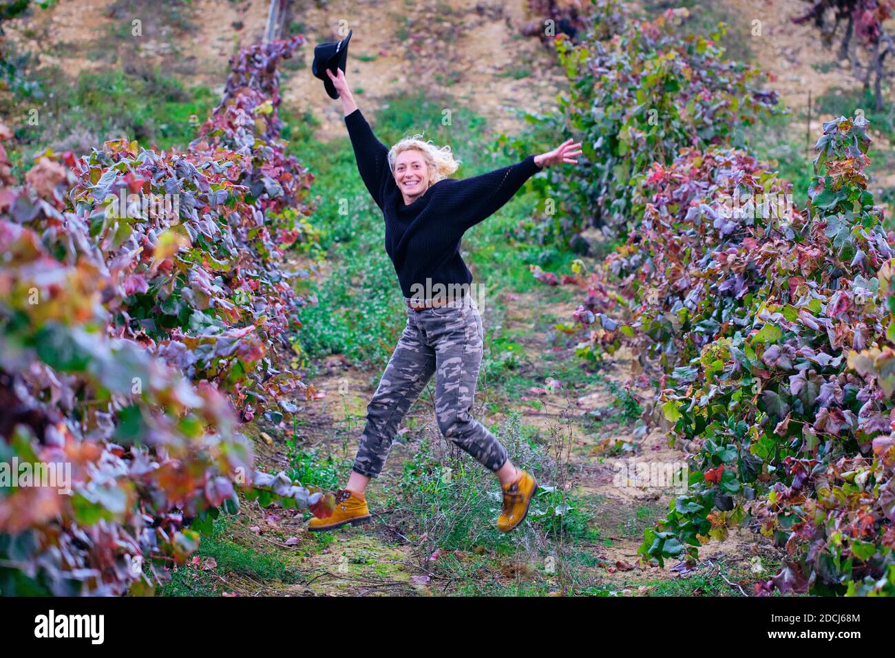 Joyful mature young blondy farmer woman jumping in a vineyard farmland. Stock Photo