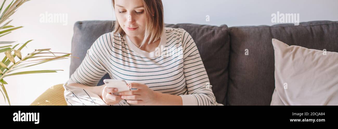 Woman sitting on couch and texting talking at social media on smartphone. Woman on sofa typing messaging on mobile phone. Chat talk with friends onlin Stock Photo