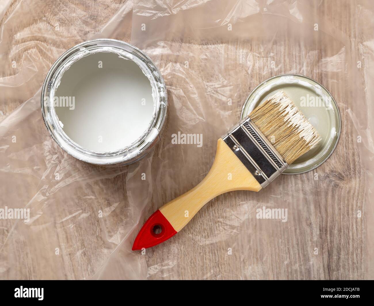 https://c8.alamy.com/comp/2DCJATB/new-natural-bristle-brush-with-paint-on-a-lid-near-an-open-paint-can-over-cellophane-covered-floor-construction-painting-work-repair-and-redecorate-2DCJATB.jpg