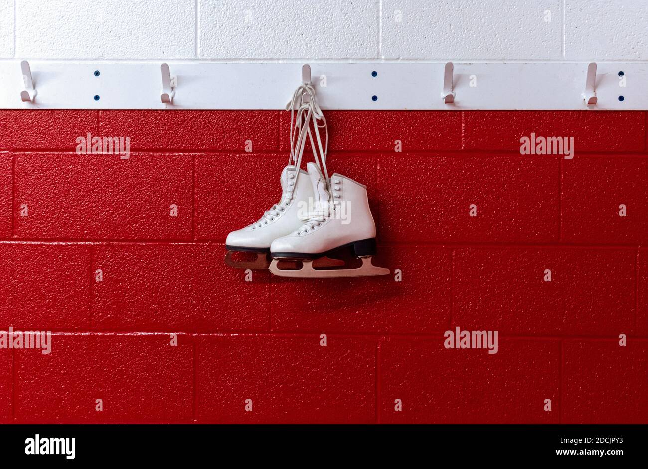 Figure skates hanging in locker room over red background with copy