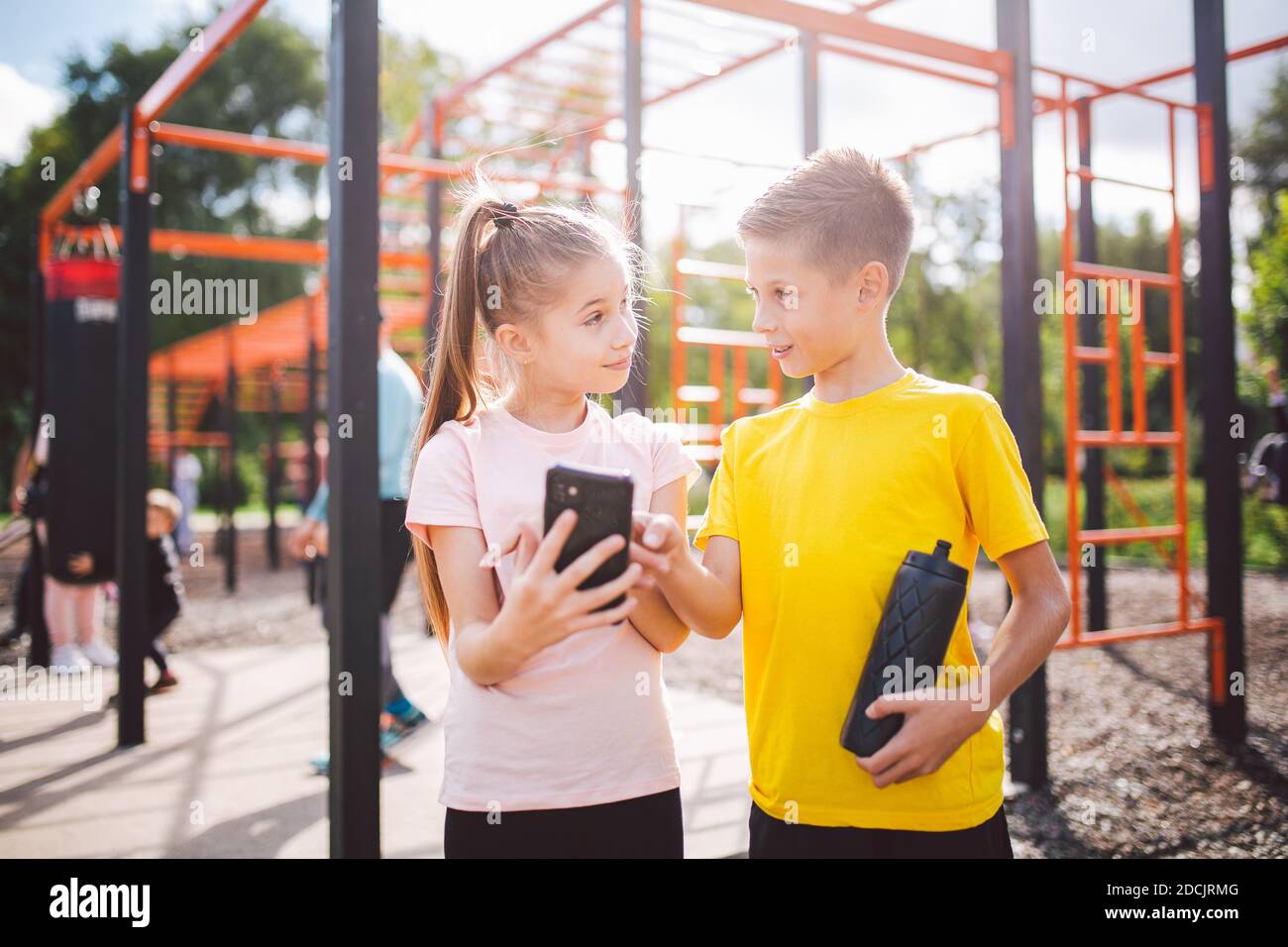 Caucasian children teenagers use cell phone in workout at street gym. Diverse twins watching video lessons with gymnastics exercises. Brother and Stock Photo