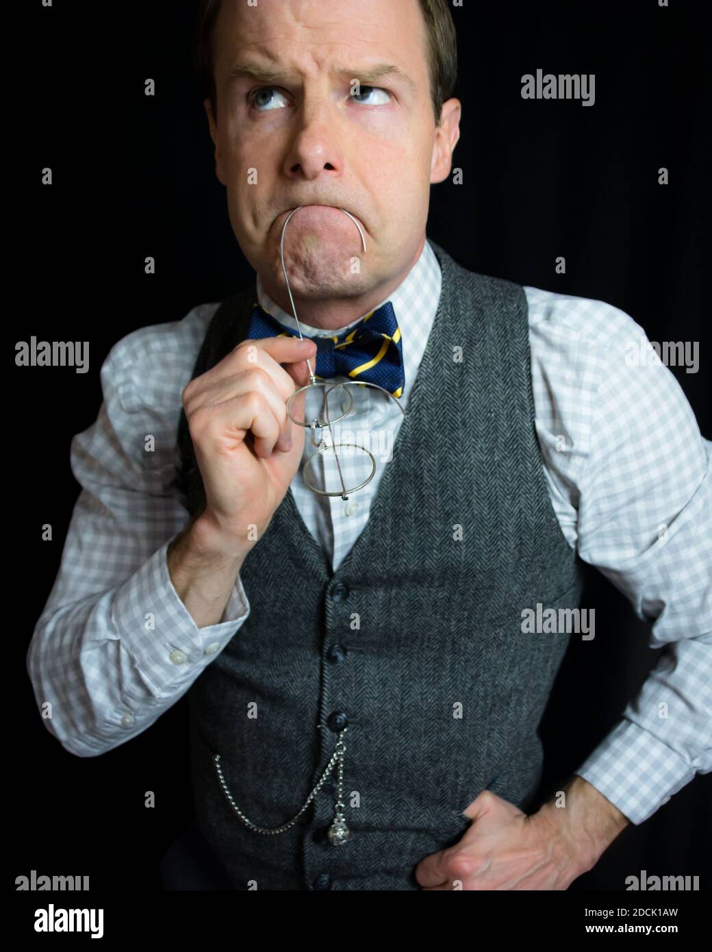 Portrait of Academic Man in Tweed Waistcoat and Bow Tie with Spectacles in His Mouth as He Ponders the Infinite. Thinking and Thoughtul. Stock Photo