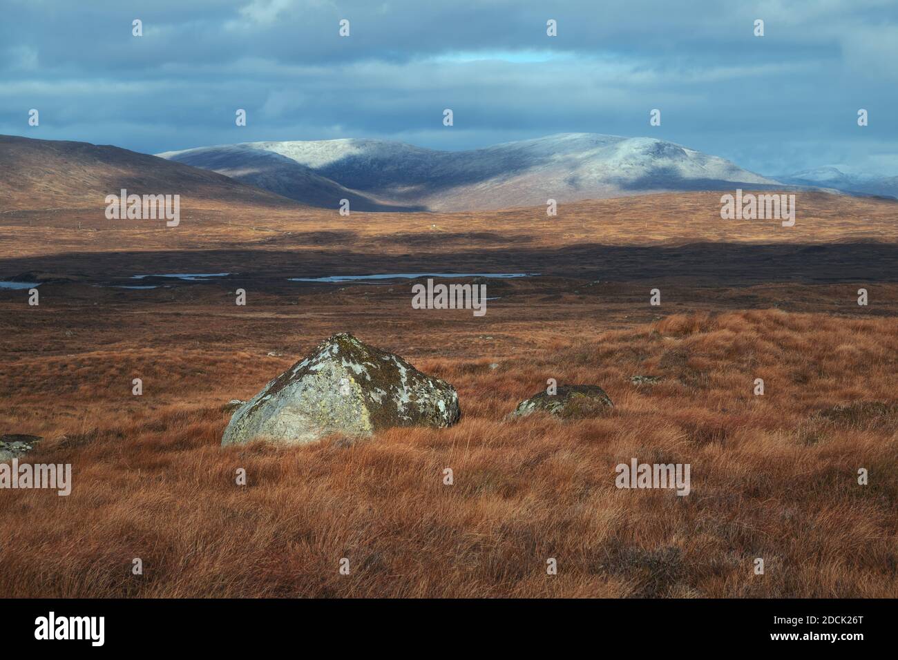 A large stone on a high-mountain plateau against a background of snowy mountain peaks. Scenic landscape autumn season view. View from the road to Glencoe. Highland, Scotland Stock Photo
