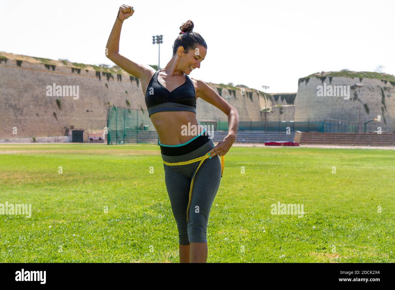 Female water sprinkled wet athlete woman in sportswear measuring her  waistline, hips and chest after a workout at an outdoor field stadium.  Healthy li Stock Photo - Alamy