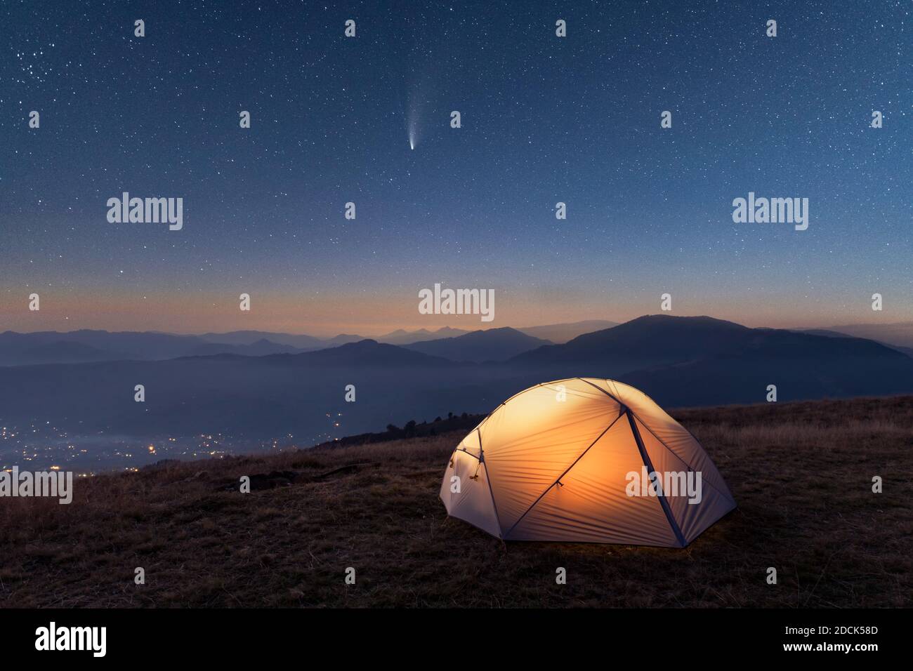 Green tent lighted from the inside by a flashlight against the backdrop of pine tree forest and glowind pink sky. Amazing snowy landscape. Tourists camp in winter mountains. Travel concept Stock Photo