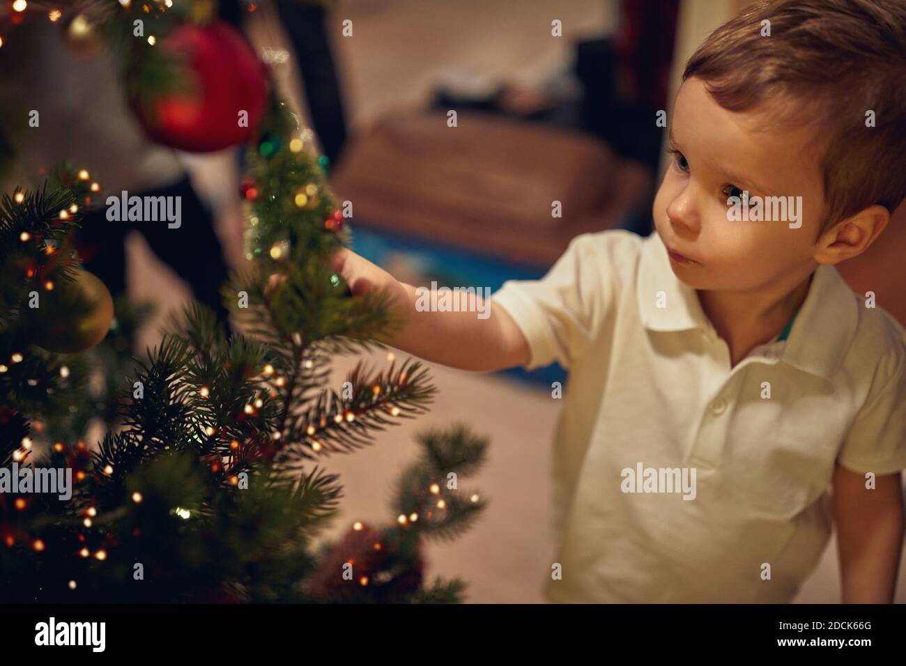A cute little kid watching ornaments on a Christmas tree in a holiday atmosphere at home. Together, New Year, family, celebration Stock Photo