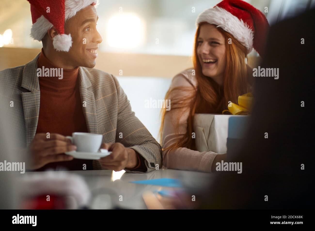young afro-american employee drinking coffee in the office talking with caucasian female colleague, wearing santa hats. christmastime Stock Photo