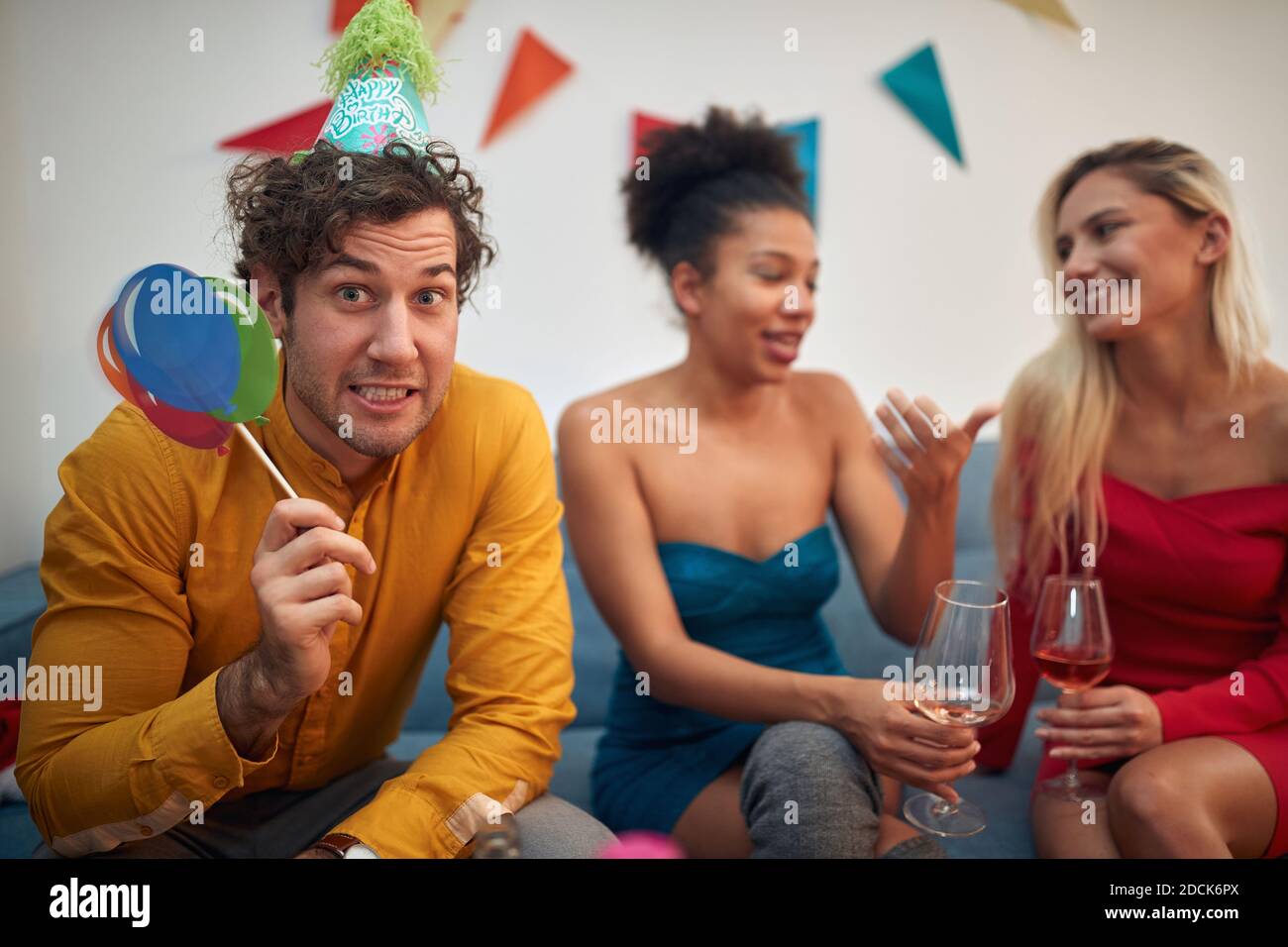 bored caucasian guy in company of two multiethnic females making funny face at the party. looking at camera, eye contact Stock Photo
